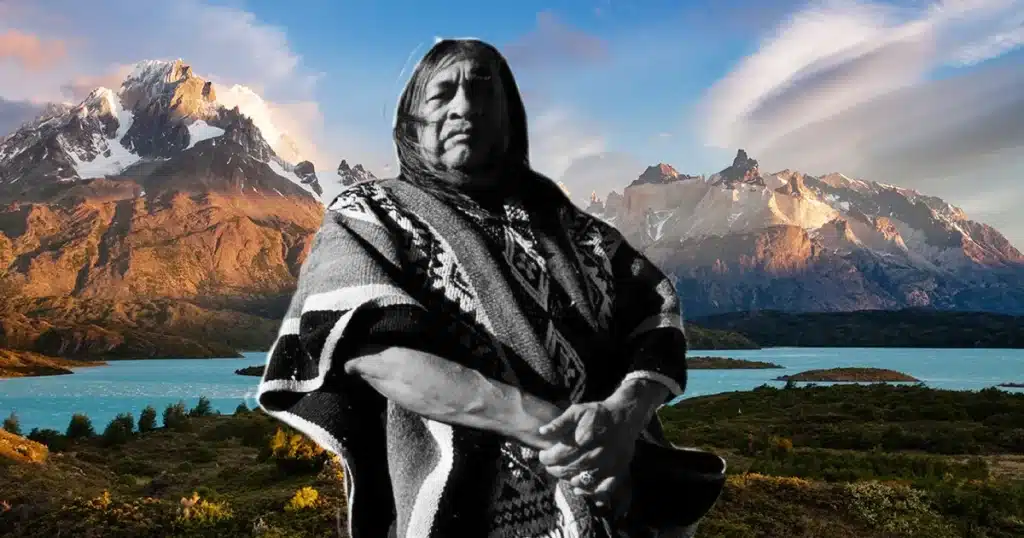 Retrato en blanco y negro de Rubén Patagonia, con fondo colorido de los Andes patagónicos, vestido con atuendo indígena tradicional.