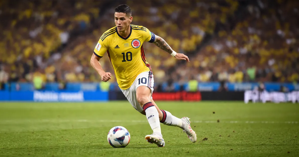 James Rodríguez con la camiseta de Colombia conduce el balón durante un partido, mostrando control y técnica con su pierna izquierda.